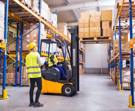 Young warehouse workers working together. Young workers working together. Man forklift driver and a woman in a warehouse.