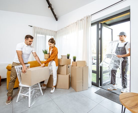 Young couple moving into a new house Young couple in the living room of their new home, mover performs professional furniture delivery during the relocation