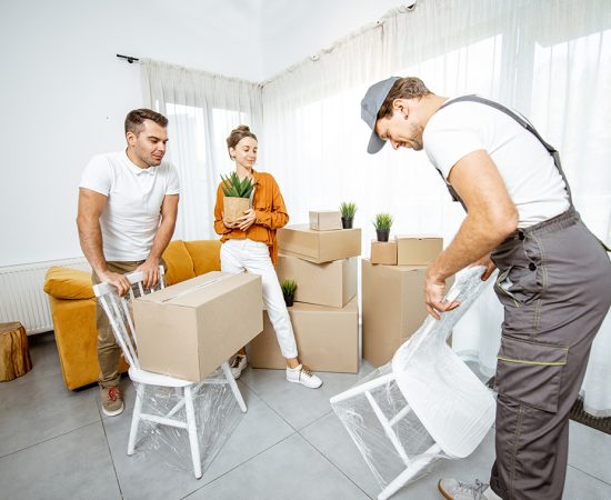 Young couple moving into a new house Young couple in the living room of their new home, mover performs professional furniture delivery during the relocation