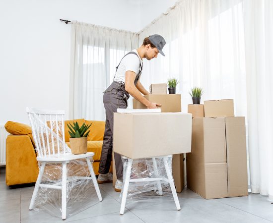 Professional mover delivering furniture to a new house Handsome mover in workwear performing professional delivery of a goods and furniture during relocation process to a new house, interior view